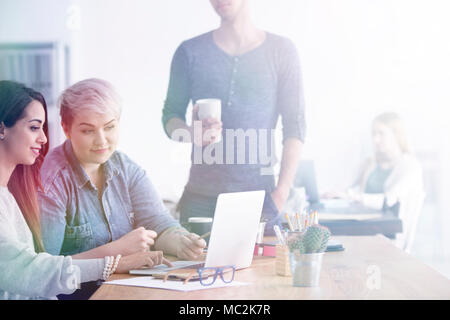 Two women sitting in an office with laptop and man standing next to them Stock Photo