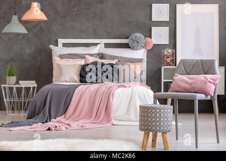 Patterned pouf and grey chair with pillow standing in cozy bedroom interior with posters Stock Photo