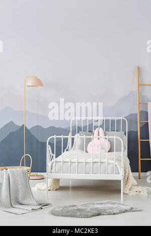 Simple, pastel pink lamp standing in bright children bedroom interior with mountain wallpaper and white bed Stock Photo