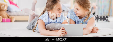 Best friends having fun together at a sleepover, playing mobile games on a tablet in girly kid's bedroom with toys Stock Photo
