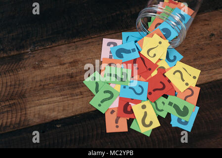 colorful paper with question mark in a plastic jar on wooden table. questions and diversity concept. FAQ and Q&A background concept Stock Photo