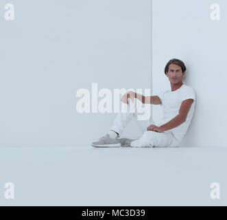 sad young man sitting beside a white wall Stock Photo