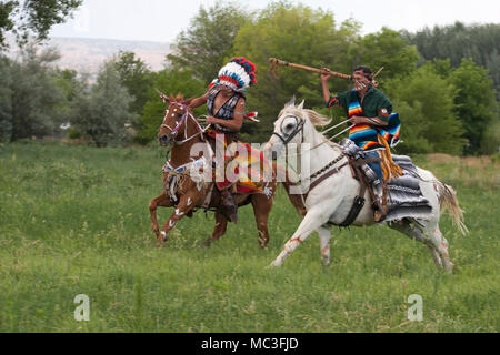 Warriors in Comanche clothing galloping horses through meadow Stock Photo