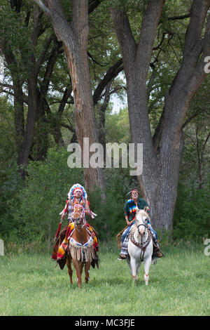 Warriors in Comanche clothing riding horses through trees in forest Stock Photo