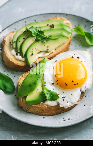 Avocado Sandwich with Fried Egg - sliced avocado and  egg on toasted bread with arugula for healthy breakfast or snack. Stock Photo