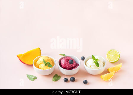 Three various fruit and berries ice creams on pink background, copy space. Frozen yogurt or ice cream with lemon, mango, blueberries - healthy summer  Stock Photo