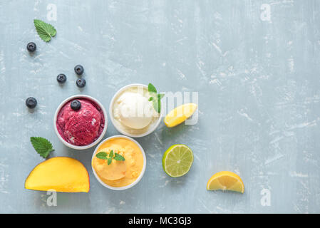 Three various fruit and berries ice creams on blue background, copy space. Frozen yogurt or ice cream with lemon, mango, blueberries - healthy summer  Stock Photo