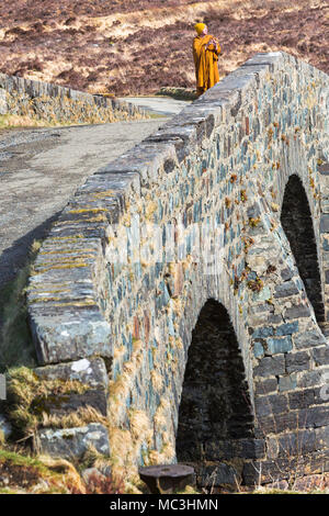 Visiting monk standing on old bridge Sligachan taking photo with phone, Isle of Skye, Scotland, UK in March Stock Photo