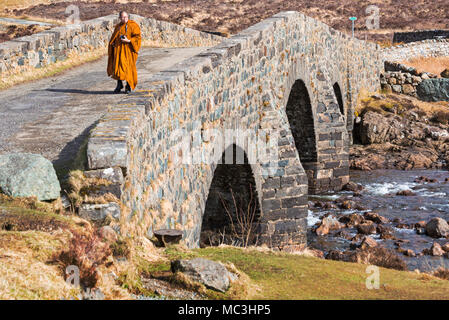 Visiting monk holding camera walking over old bridge Sligachan, Isle of Skye, Scotland, UK in March Stock Photo