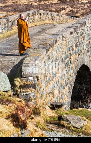 Visiting monk standing on old bridge Sligachan taking a photo, Isle of Skye, Scotland, UK in March Stock Photo