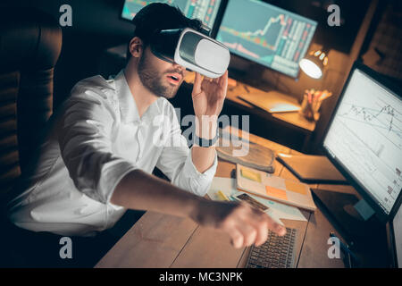 Excited businessman wearing vr headset working in ar trading on stock market, trader using glasses headset goggles touching cyberspace objects on inte Stock Photo