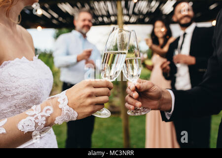 Close up of bride and groom toasting champagne glasses at wedding party. Newlyweds clinking glasses at wedding reception outside. Stock Photo