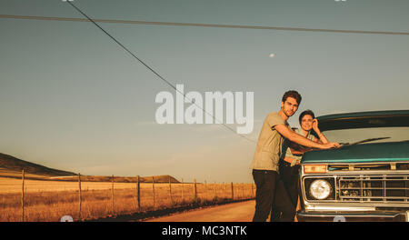 Couple standing beside their car on a highway in country side. Man and woman on a road trip. Stock Photo