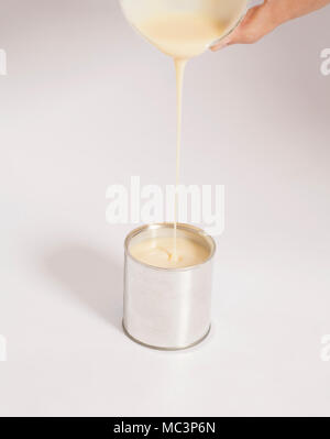 Male hand pouring condensed milk into a tin can on white Stock Photo