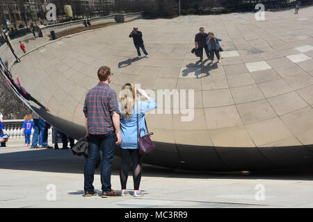 A young couple pose for selfies with Chicago's 'Bean' in Millennium Park on a warm spring day. Stock Photo