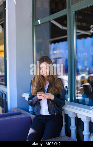 Young woman typing by smartphone at street cafe. Stock Photo