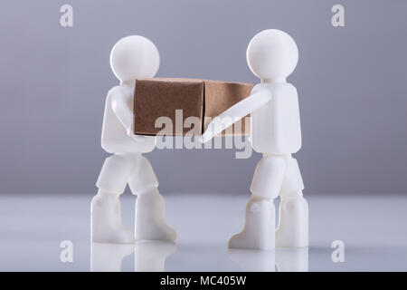 Close-up Two Human Figures Carrying Cardboard Box Against Grey Background Stock Photo