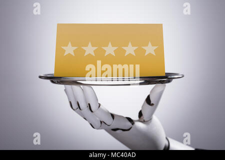 Close-up Of A Robotic Hand Holding Plate With Star Rating On Grey Background Stock Photo