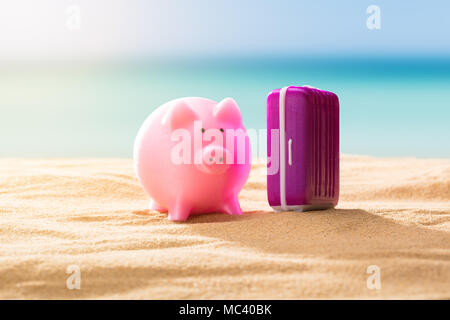 Close-up Of Pink Piggy Bank And Luggage On Sandy Beach Stock Photo
