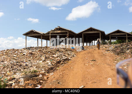 Jinja, Uganda. 21 May 2017. Two relatively well dressed Ugandan walking on dirt road through a large landfill. Shot from a 'boda boda' motorbike. Stock Photo