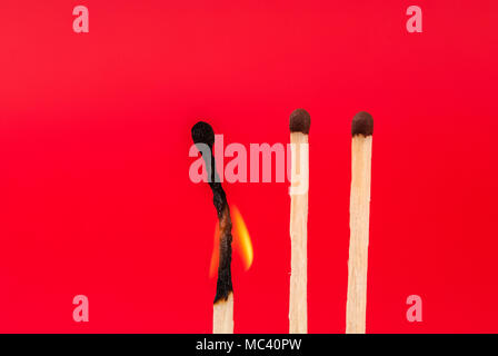 Three matches and one burned on red background Stock Photo