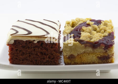 Side by side square slices of two different cakes, raspberry crumb cake and red velvet cake, on white plate in close up photograph. Stock Photo