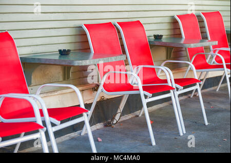 Red and white chairs and tables line the sidewalk, secured to the wall of a building, in this urban setting . Stock Photo