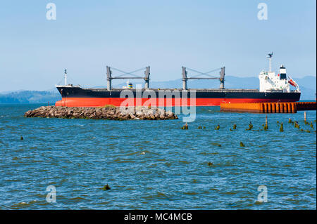 A huge freighter, near the river banks, heads out toward the Pacific Ocean by way of the Columbia River in Astoria Oregon. Stock Photo