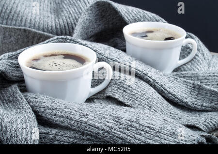 Two cups of hot coffee in the folds of a gray scarf close-up with shallow depth of focus Stock Photo