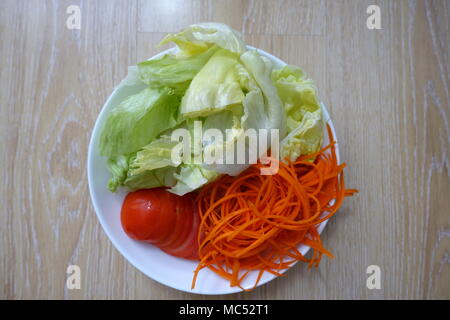 Iceberg lettuce, shredded carrot and tomato slices on white plate against wooden backgorund Stock Photo