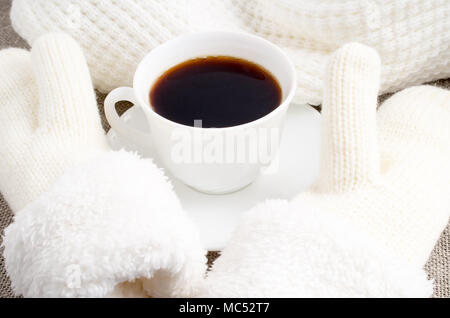 White cup with hot coffee next to the white woolen mittens and a scarf Stock Photo