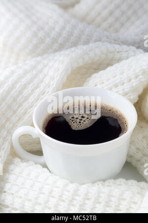 White cup with hot coffee wrapped in a white woolen scarf with shallow depth of focus. Stock Photo