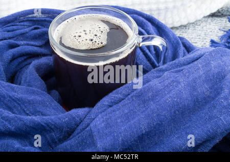 Transparent glass mug with coffee wrapped in blue cotton scarf close-up Stock Photo