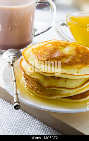 A mug of cocoa, silver spoon, honey and pancakes for dessert closeup with shallow depth of field. Stock Photo