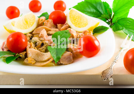 Salad of blanched pieces of seafood on a white plate close-up. Mussels, squid and octopus, decorated with greens, cherry and lemon. Stock Photo