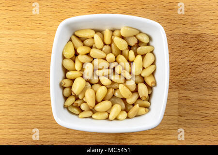 Overhead shot of raw pine nuts in a white bowl on a wooden chopping board background Stock Photo
