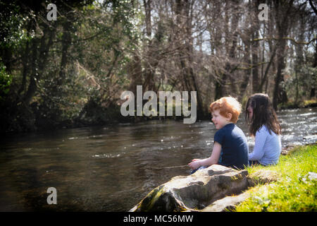 A boy and a girl playing at fishing, on the banks of the River Crake at Spark Bridge.