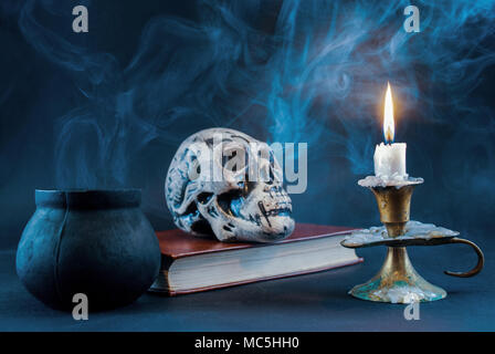 Candle burning and witch pot smoking and skull on book in background, dark and smoked scene. Halloween concept. Stock Photo