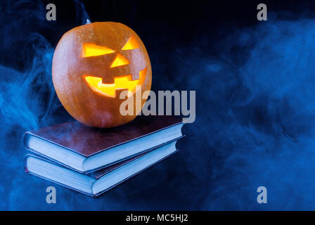 Halloween pumpkin with candle on old books and smoked and dark background Stock Photo