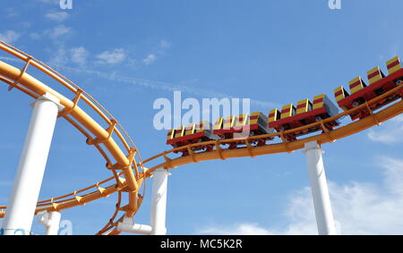 Abstract-style shot of the yellow roller-coaster at Pacific Park, Santa Monica against a blue sky with white clouds. No people visible in image Stock Photo