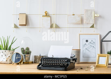 A golden frame organizer on a white wall above a desk with vintage, black typewriter, succulents, frames and decorations Stock Photo