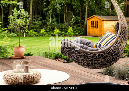 Pouf on white round rug next to a hanging chair in the garden of a house Stock Photo