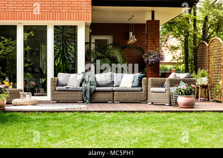 Grey pillows and blanket on garden furniture in front of a house in the summer Stock Photo