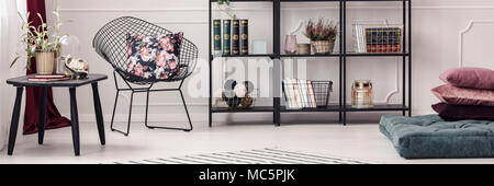 Panorama of a luxurious apartment interior with wire chair, pillows, black bookcase and elegant decorations Stock Photo