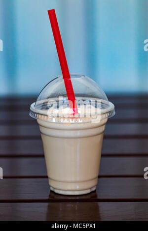 Vanilla milkshake covered with whipped cream in plastic glass on wooden background. Stock Photo
