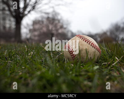 Close up sports background image of an old used weathered leather baseball ball laying in the grass field outside showing intricate detail and texture Stock Photo