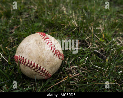 Close up sports background image of an old used weathered leather baseball ball laying in the grass field outside showing intricate detail and texture Stock Photo