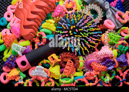 On multi-colored colorful elastic bands for hair lies a comb and hair clip on a black background. Stock Photo