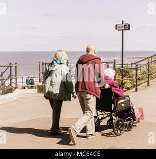 Couple and elderly woman in wheelchair near beach uk. Caring for elderly parent/person... Stock Photo