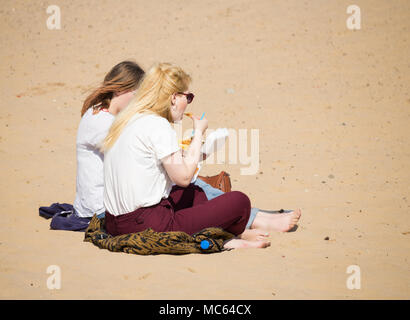 Two young women eating fish and chips on the beach. England. UK Stock Photo